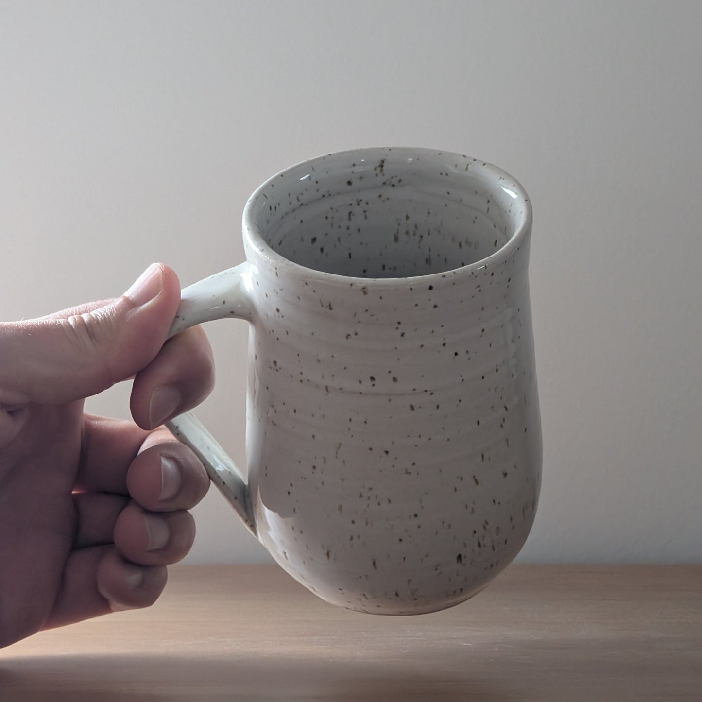 Hand holding a speckled ceramic mug against a plain background