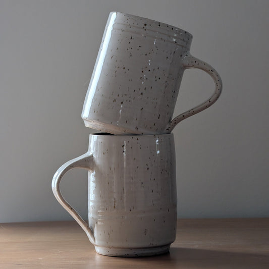Two stacked ceramic mugs on a wooden surface with a plain background