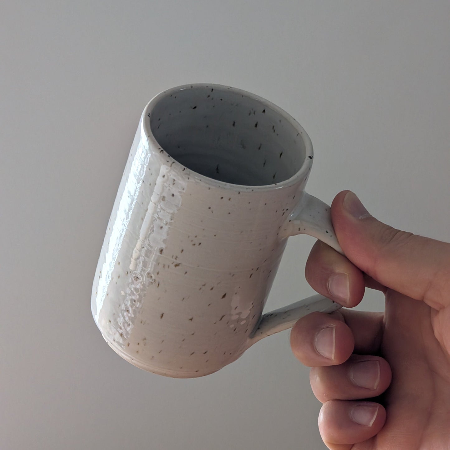 Hand holding a speckled ceramic mug against a plain background