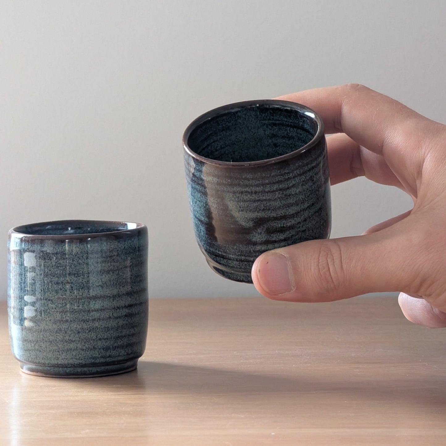 Hand holding a dark blue ceramic cup on a light wooden surface with a plain background