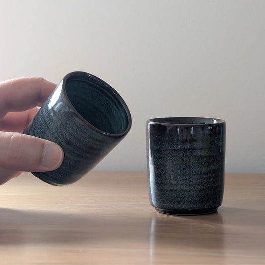 Two blue ceramic cups on a wooden surface with a plain background