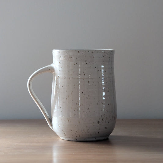 Speckled ceramic mug on a wooden surface with a plain background