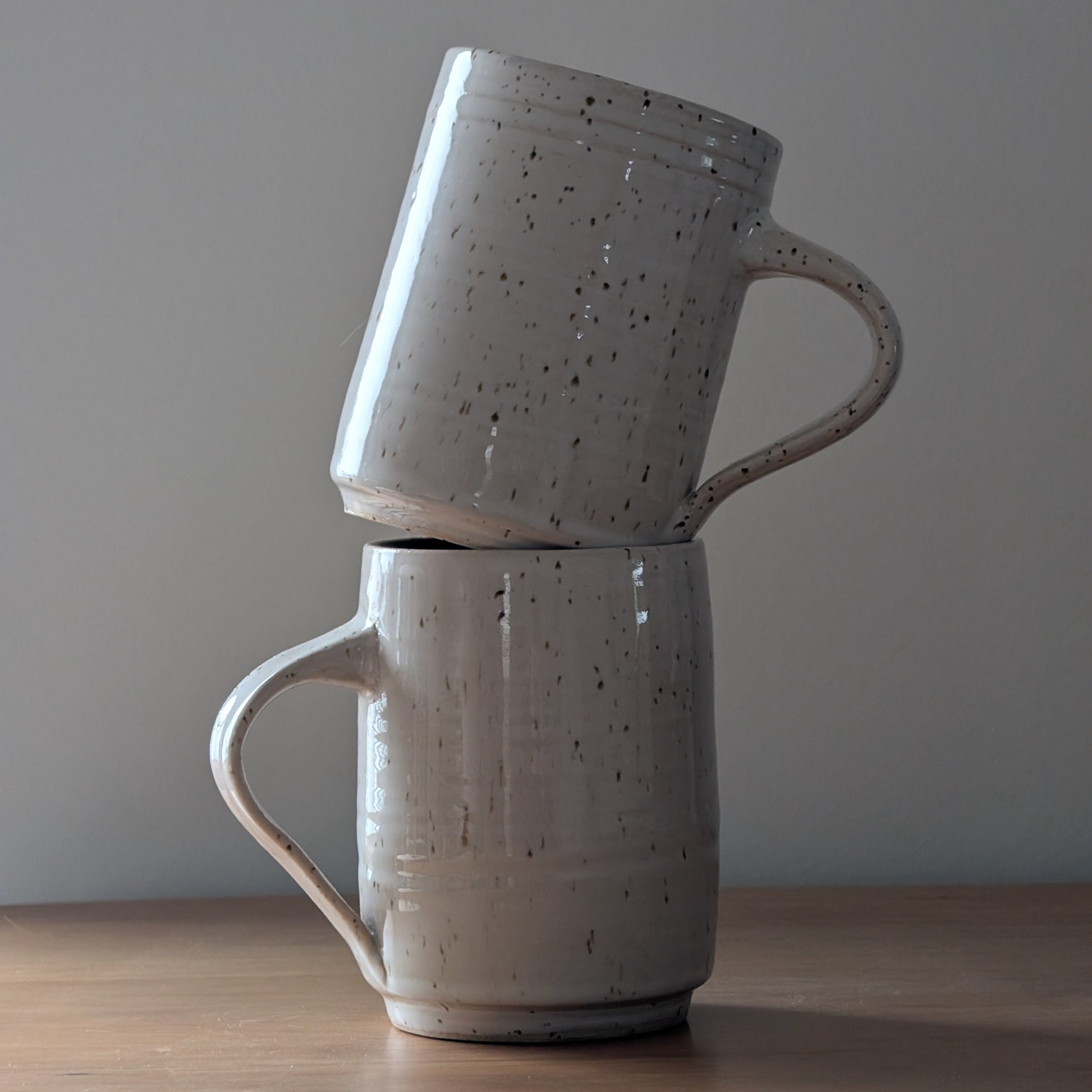 Two stacked ceramic mugs on a wooden surface with a plain background