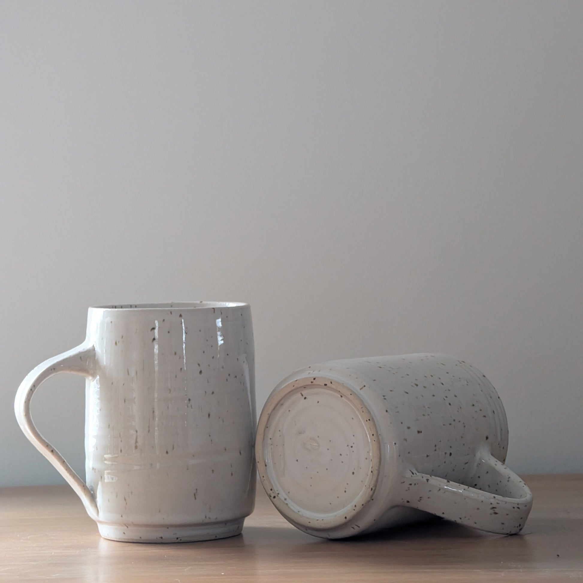 Two ceramic mugs on a wooden surface with a plain background