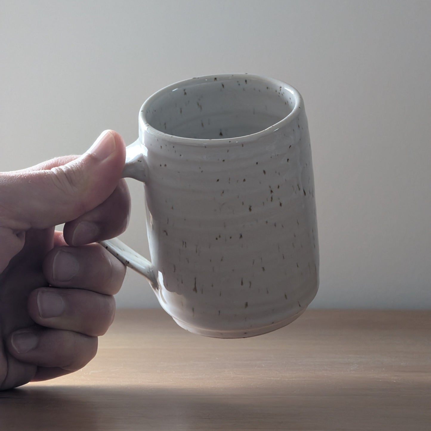 Hand holding a speckled ceramic mug against a plain background