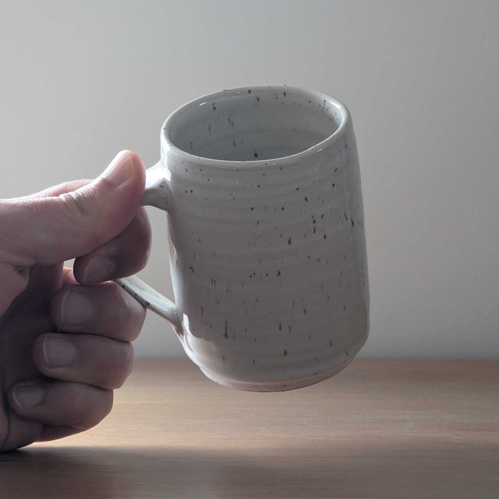 Hand holding a speckled ceramic mug against a plain background