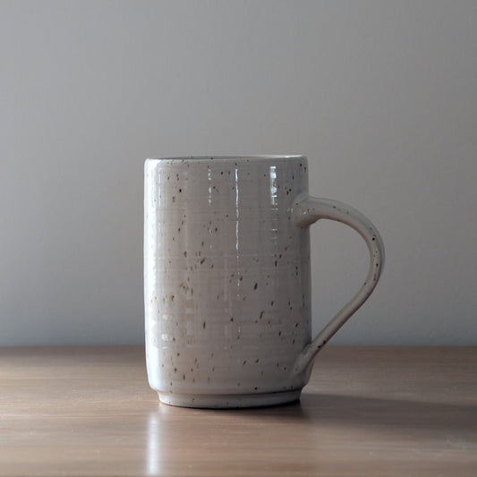 Speckled ceramic mug on a wooden surface with a plain background