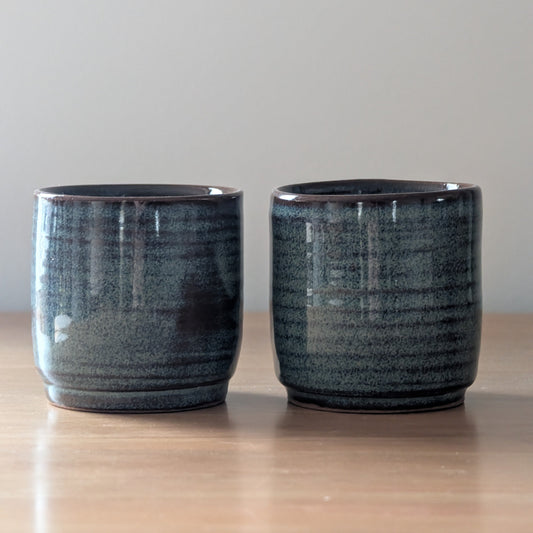 Two dark blue ceramic cups on a wooden surface with a light gray background