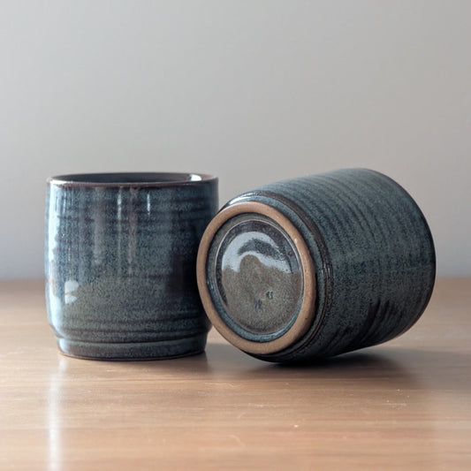 Two dark blue ceramic containers on a wooden surface with a light gray background