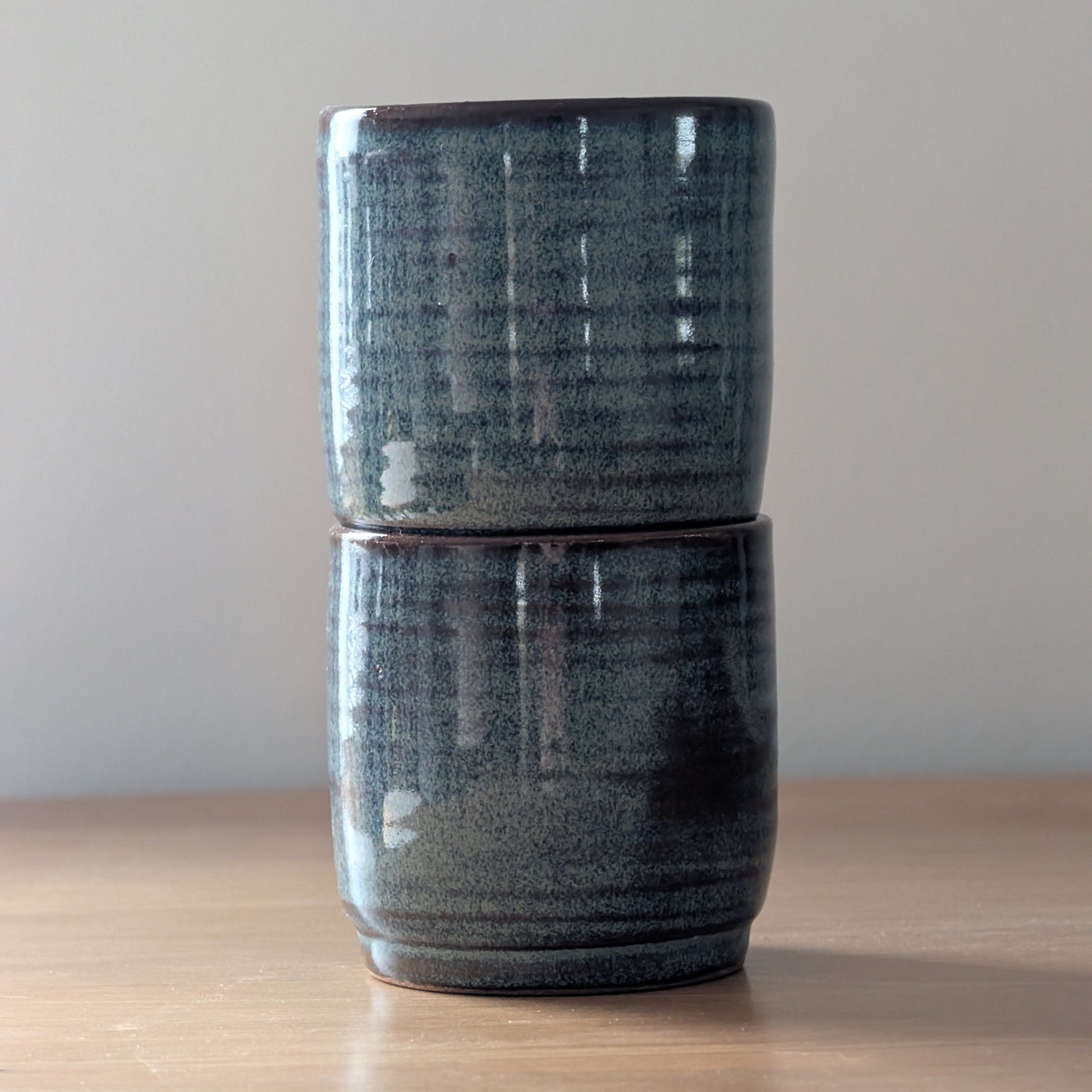Two stacked ceramic tumblers on a wooden surface with a plain background
