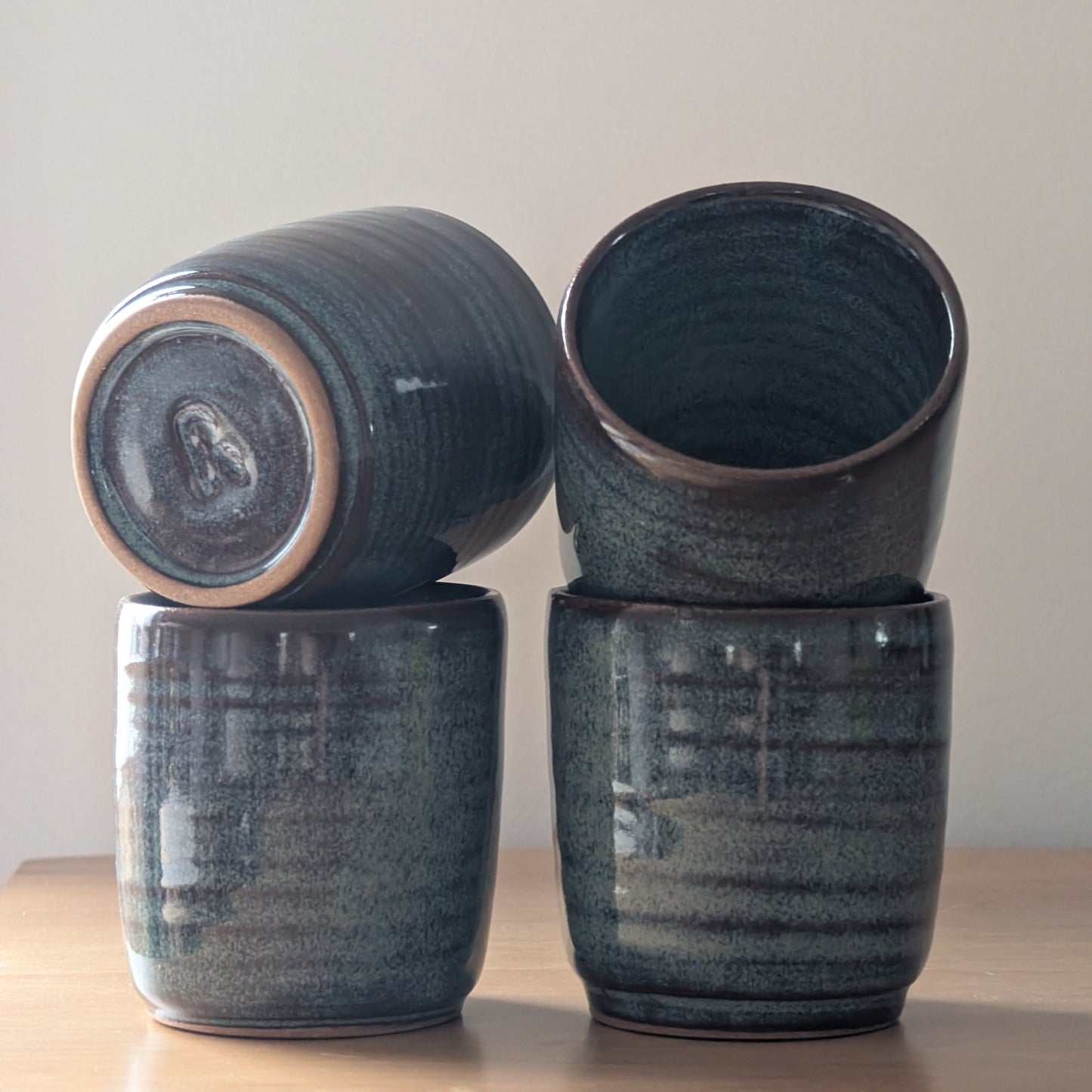Four dark blue ceramic cups stacked on a light wooden surface with a plain background