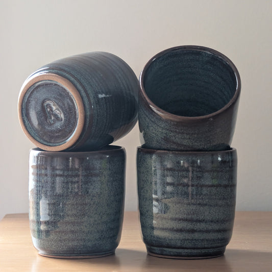 Four dark blue ceramic cups stacked on a light wooden surface with a plain background