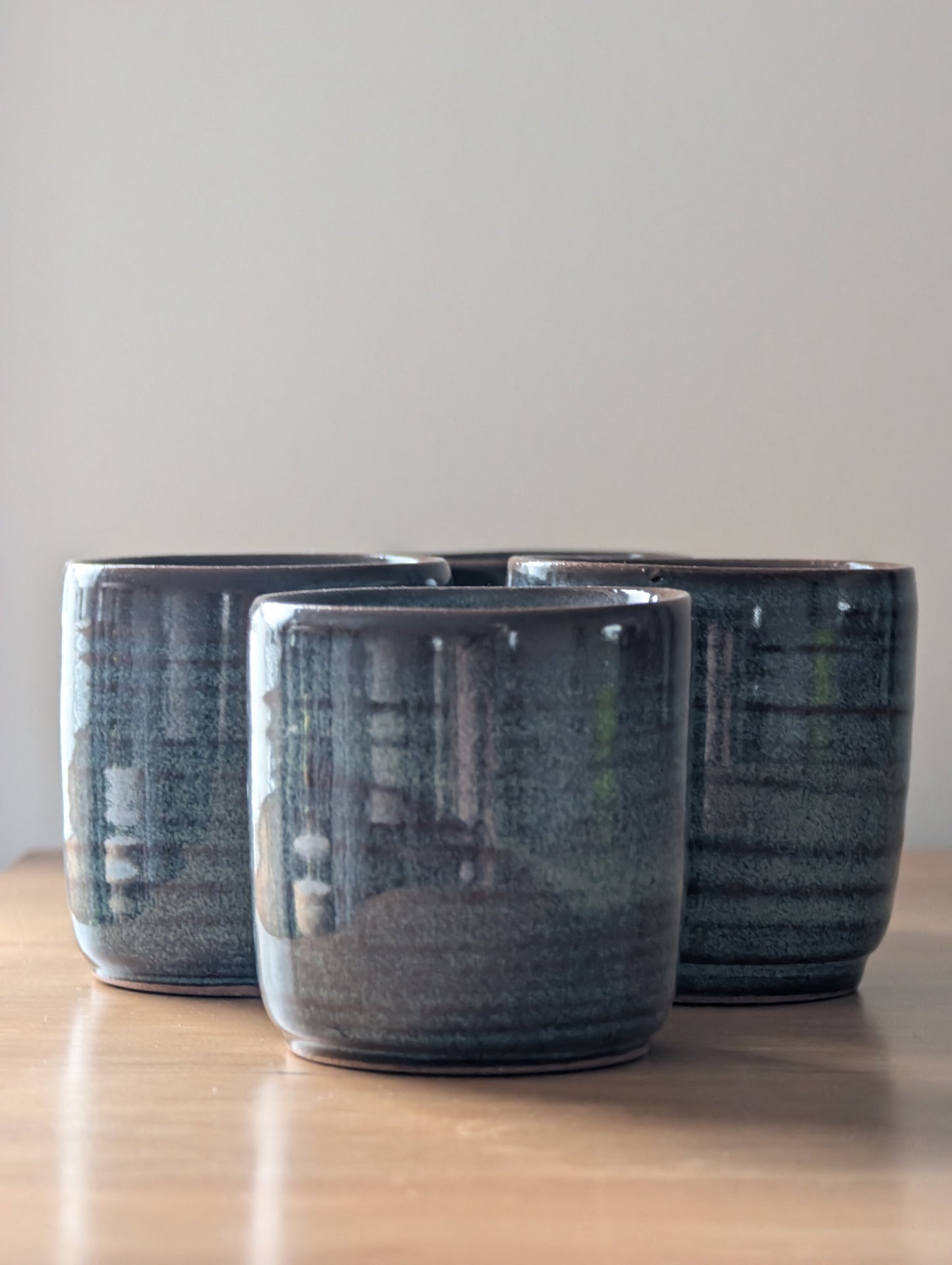 Three dark blue ceramic cups on a light wooden surface with a plain background