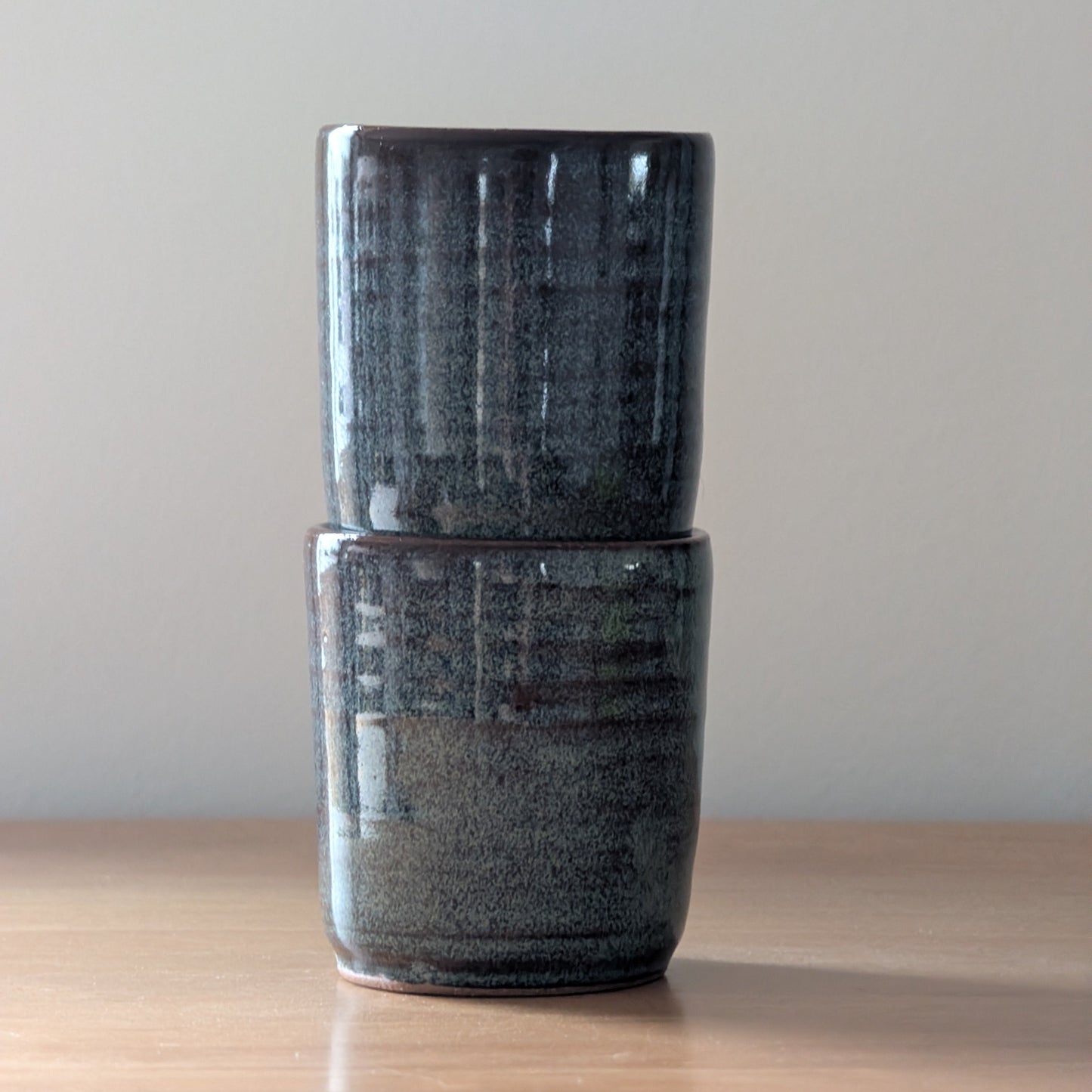 Two dark ceramic cups stacked on a wooden surface with a plain background